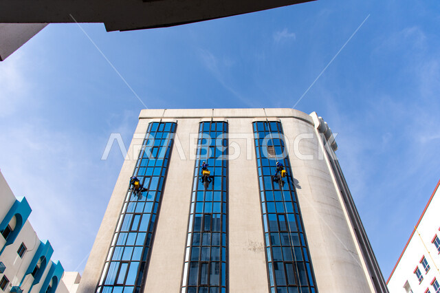 خدمة التنظيف في العمارات المرتفعة، الفن الهندسي المعماري للأبراج وناطحات السحاب، المنشآت الحديثة بديكورات وتصاميم متميزة في الإمارات العربية المتحدة، عمال عرب خليجيين إماراتيين يقومون بتنظيف الزجاج الخارجي لبناء مرتفع شاهق