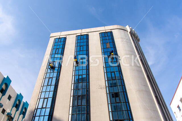 خدمة التنظيف في العمارات المرتفعة، الفن الهندسي المعماري للأبراج وناطحات السحاب، المنشآت الحديثة بديكورات وتصاميم متميزة في الإمارات العربية المتحدة، عمال عرب خليجيين إماراتيين يقومون بتنظيف الزجاج الخارجي لبناء مرتفع شاهق