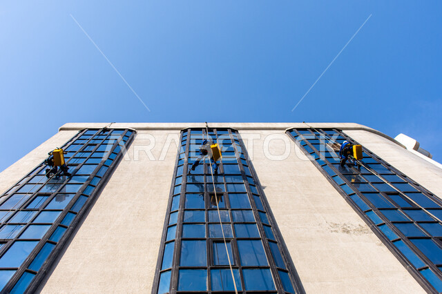 خدمة التنظيف في العمارات المرتفعة، الفن الهندسي المعماري للأبراج وناطحات السحاب، المنشآت الحديثة بديكورات وتصاميم متميزة في الإمارات العربية المتحدة، عمال عرب خليجيين إماراتيين يقومون بتنظيف الزجاج الخارجي لبناء مرتفع شاهق