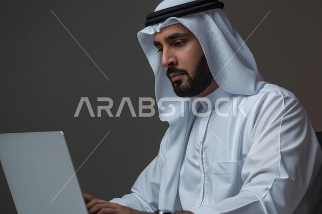 إدارة شؤون الأعمال وتنظيمها عبر الاجهزة التقنية، دمج العمل مع التقنية والتكنولوجيا، بورتريه مقرب لرجل اعمال عربي خليجي سعودي يرتدي الزي التقليدي والغترة يعمل على جهاز الحاسوب المحمول بإيماءات التركيز، مهن ووظائف ادارية مكتبية، خلفية رمادية