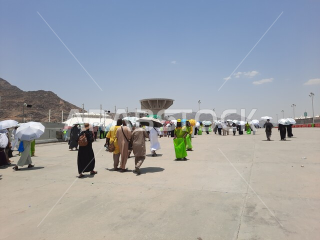 مجموعة من الحجاج والمعتمرين يحملون المظلات ويسيرون في منطقة رمي الجمرات في مكة المكرمة, أداء مناسك الحج والعمرة, أماكن إسلامية مقدسة, زيارة بيت الله الحرام