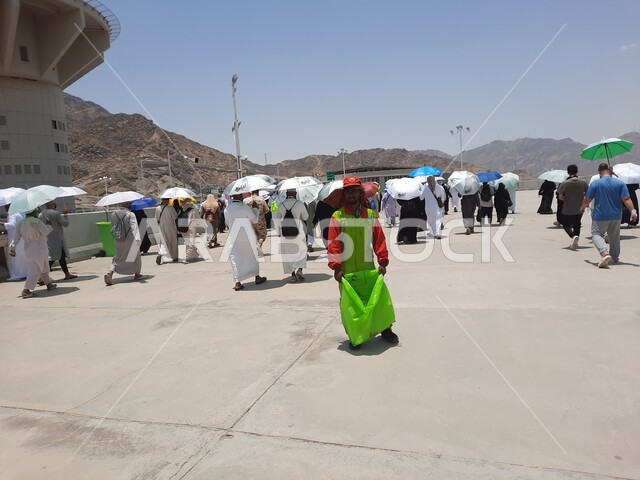 مجموعة من الحجاج والمعتمرين يحملون المظلات ويسيرون في منطقة رمي الجمرات في مكة المكرمة, أداء مناسك الحج والعمرة, أماكن إسلامية مقدسة, زيارة بيت الله الحرام