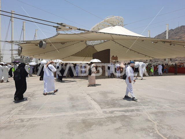 مجموعة من الحجاج والمعتمرين يقفون تحت الشمسية في منطقة رمي الجمرات في مكة المكرمة, أداء مناسك الحج والعمرة, أماكن إسلامية مقدسة, مفهوم العبادة و التقرب من الله تعالى