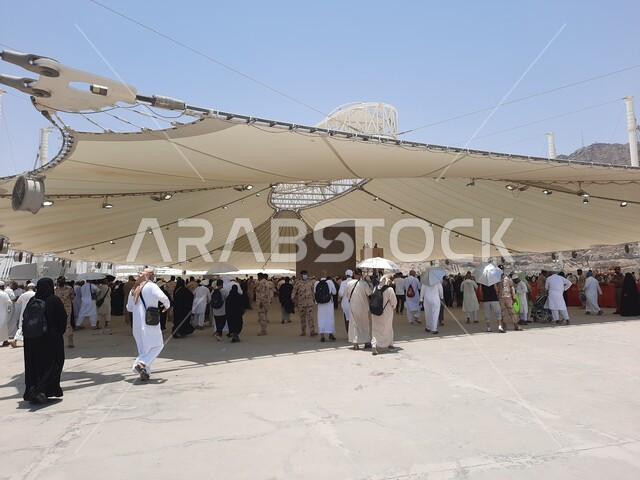 مفهوم العبادة و التقرب من الله تعالى, مجموعة من الحجاج والمعتمرين يقفون تحت الشمسية في منطقة رمي الجمرات في مكة المكرمة, أداء مناسك الحج والعمرة, أماكن إسلامية مقدسة