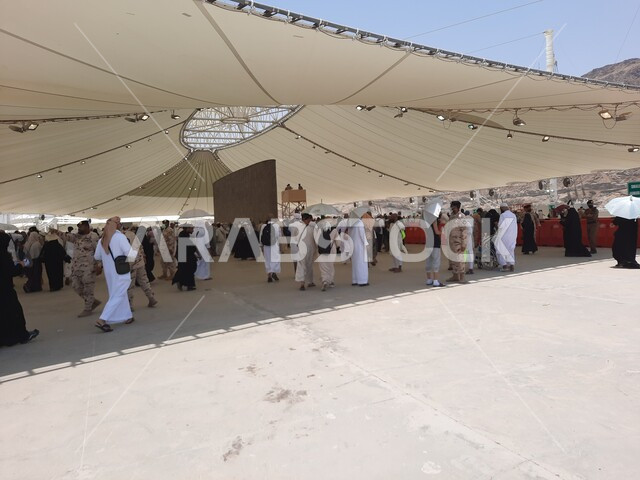 مجموعة من الحجاج والمعتمرين يقفون تحت الشمسية في منطقة رمي الجمرات في مكة المكرمة، أداء مناسك الحج والعمرة، أماكن إسلامية مقدسة, مفهوم العبادة و التقرب من الله تعالى