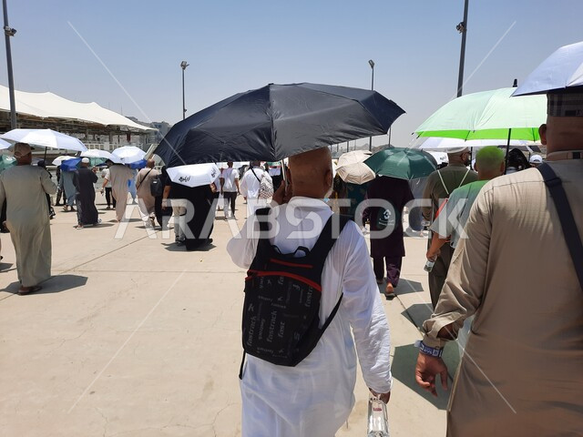 الحجاج المسلمين يقومون بأداء مناسك الحج والعمرة, أماكن إسلامية دينية مقدسة في المملكة العربية السعودية, العبادة و التقرب إلى الله تعالى, زوار بيت الله الحرام يسيرون في منطقة جسر الجمرات في مكة المكرمة و يحملون المظلات