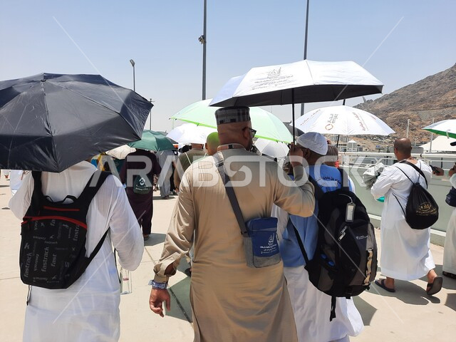 زوار بيت الله الحرام يسيرون في منطقة جسر الجمرات في مكة المكرمة و يحملون المظلات, الحجاج المسلمين يقومون بأداء مناسك الحج والعمرة, أماكن إسلامية دينية مقدسة في المملكة العربية السعودية, العبادة و التقرب إلى الله تعالى