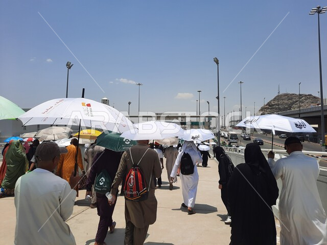 الحجاج المسلمين يقومون بأداء مناسك الحج والعمرة, أماكن إسلامية دينية مقدسة في المملكة العربية السعودية, العبادة و التقرب إلى الله تعالى, زوار بيت الله الحرام يسيرون في منطقة جسر الجمرات في مكة المكرمة و يحملون المظلات