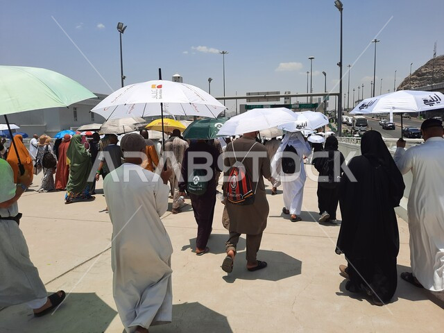 زوار بيت الله الحرام يسيرون في منطقة جسر الجمرات في مكة المكرمة و يحملون المظلات, الحجاج المسلمين يقومون بأداء مناسك الحج والعمرة, أماكن إسلامية دينية مقدسة في المملكة العربية السعودية, العبادة و التقرب إلى الله تعالى