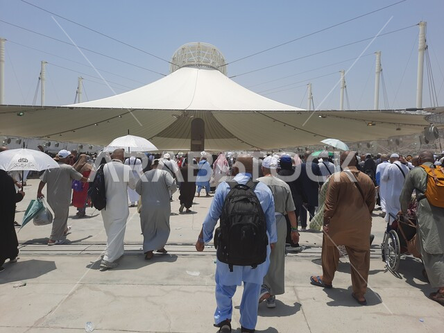 مجموعة من الحجاج والمعتمرين يسيرون تحت المظلات في منطقة رمي الجمرات في مكة المكرمة، زوار بيت الله الحرام يقومون بأداء مناسك الحج والعمرة، أماكن إسلامية دينية مقدسة, مفهوم العبادة و التقرب من الله تعالى