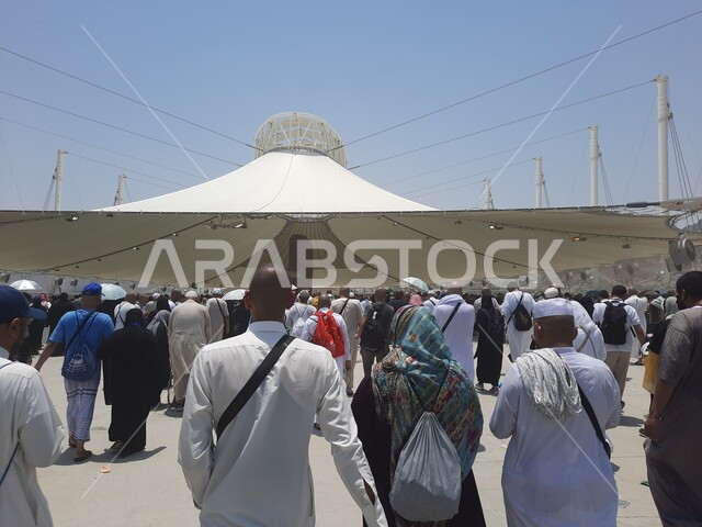 مجموعة من الحجاج والمعتمرين يسيرون تحت المظلات في منطقة رمي الجمرات في مكة المكرمة، زوار بيت الله الحرام يقومون بأداء مناسك الحج والعمرة، أماكن إسلامية دينية مقدسة, مفهوم العبادة و التقرب من الله تعالى