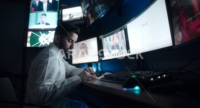 Television media, integrating the practical environment with technique and technology, a Saudi Gulf Arab man wearing the traditional dress and shemagh looks at the camera with confident gestures, recording notes and monitoring television stations.