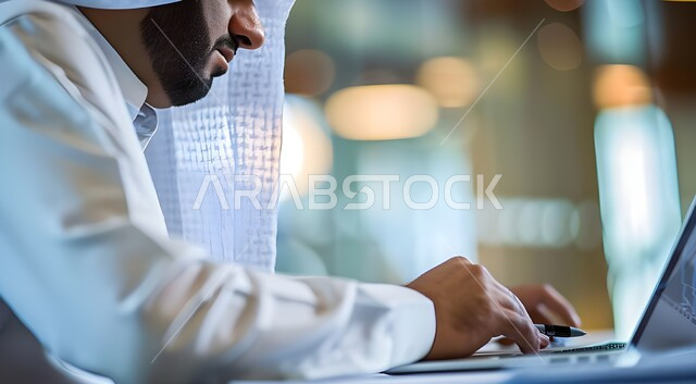 استكمال الأعمال والمهام عبر الكمبيوتر، صورة جانبية لرجل سعودي خليجي عربي يرتدي الثوب ويضع الغترة, التفكير والاستنتاج والعمل على الحاسب المحمول داخل مكتب العمل بمقر الشركة، تكامل العمل مع التقنية والتقنية، المهن والوظائف السعودية