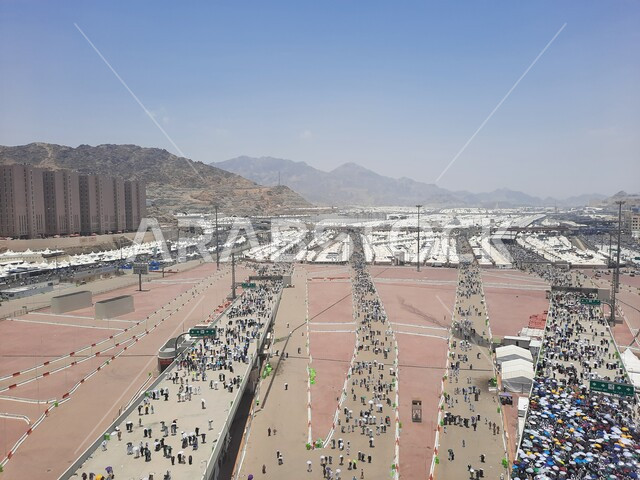 زوار بيت الله الحرام يسيرون في منطقة جسر الجمرات في مكة المكرمة و يحملون المظلات, أماكن إسلامية دينية مقدسة في المملكة العربية السعودية, العبادة و التقرب إلى الله تعالى, الحجاج المسلمين يقومون بأداء مناسك الحج والعمرة