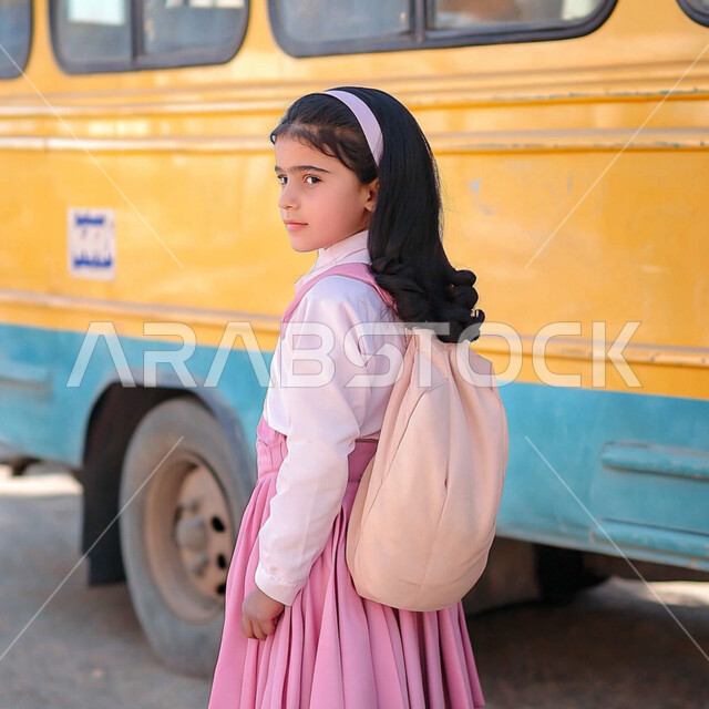 Expressions of politeness and morals, love of learning and education, a Saudi Arabian Gulf student wearing a uniform and standing next to a school bus, preparing for the new school year, returning to school, looking at the camera with gestures of happiness and pleasure, diligence and perseverance to reach higher ranks