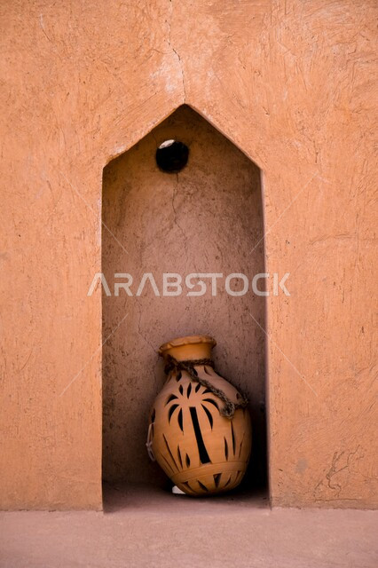 مهن وصناعات يدوية شعبية تراثية قديمة،  صورة فخارة تقليدية مزخرفة امام حائط طيني، بيع أواني الفخار في سوق شعبي تقليدي في المملكة العربية السعودية، الأواني والمنتجات الفخارية المصنوعة من الطين