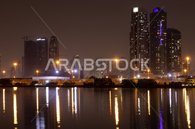 الفن الهندسي المعماري في بناء الأبراج وناطحات السحاب على شاطئ الممزر, الواجهة البحرية الساحلية في مدينة دبي, انعكاس الأضواء والأنوار للفنادق والمباني على مياه البحر في وقت الليل، النمو والتطور العمراني في الامارات العربية المتحدة, وجهات جذب واستقطاب السياح