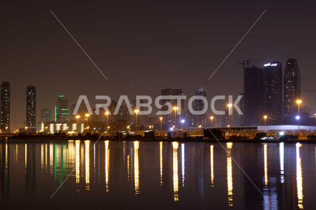 الفن الهندسي المعماري في بناء الأبراج وناطحات السحاب على شاطئ الممزر, الواجهة البحرية الساحلية في مدينة دبي, انعكاس الأضواء والأنوار للفنادق والمباني على مياه البحر في وقت الليل، النمو والتطور العمراني في الامارات العربية المتحدة, وجهات جذب واستقطاب السياح