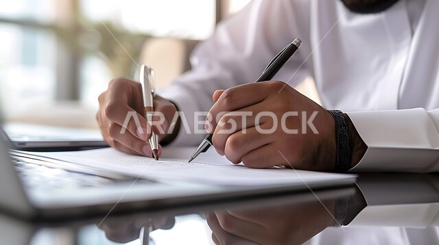  ملفات ووثائق خاصة بالعمل, مهن ووظائف مكتبيه, صورة مقربة ليد رجل عربي خليجي سعودي يرتدي الثوب التقليدي  يقوم بتدوين وكتابة الملاحظات على الورق , متابعه اعمال الشركه ودراسه وتتبع المشاريع , انجاز المهام وتحقيق الاهداف