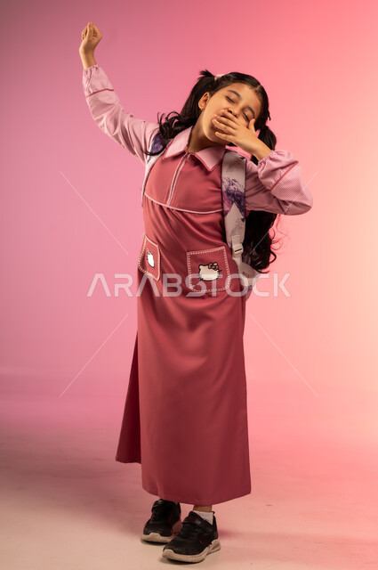 الحاجة إلى الراحة و النوم, مفهوم العودة إلى المدارس, التعليم في المملكة العربية السعودية, بورتريه لفتاة عربية خليجية سعودية ترتدي الزي المدرسي تضع يدها على فمها بتعابير التثاؤب و النعاس, الجسم بالطول الكامل, خلفية ملونة