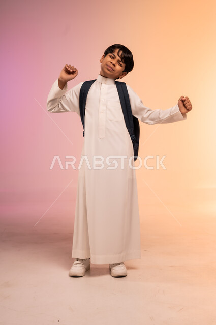  الاستعداد للذهاب إلى المدرسة، بورتريه لطالب عربي خليجي سعودي يرتدي الثوب التقليدي يحمل حقيبة الظهر المدرسية يرفع يديه بإيماءات النعاس والكسل، الحاجة إلى النشاط والتركيز، موسم العودة للمدارس في المملكة العربية السعودية، صورة الجسم بالطول الكامل، خلفية ملونة