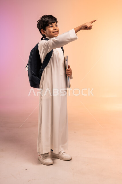 الإشارة باليد إلى شيء ما بعيد، موسم العودة إلى المدارس، الجد والاجتهاد للوصول إلى النجاح والتفوق، بورتريه لطالب عربي خليجي سعودي يرتدي الثوب التقليدي يحمل حقيبة الظهر المدرسية ينظر للأعلى بإيماءات التركيز والاندماج، الجسم بالطول الكامل، خلفية ملونة