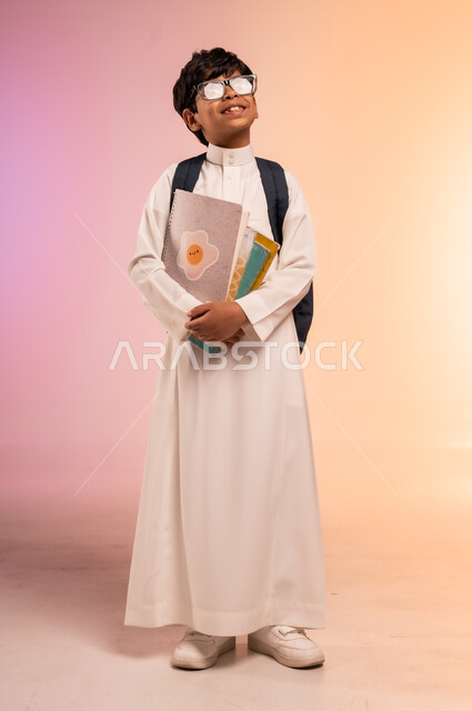 التطلع نحو النجاح والتفوق، موسم العودة إلى المدارس، بورتريه لطالب عربي خليجي سعودي يرتدي الثوب التقليدي ويضع نظارة طبية يحمل حقيبة الظهر المدرسية، الإمساك بالكتب والمناهج التعليمية والنظر للأعلى بإيماءات الاندماج، الجسم بالطول الكامل، خلفية ملونة