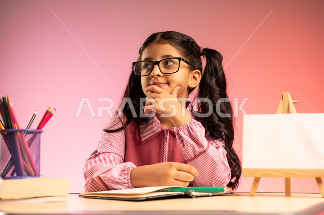 الجد والاجتهاد للوصول إلى النجاح والتفوق، موسم العودة إلى المدارس، بورتريه لطالبة عربية خليجية سعودية ترتدي الزي المدرسي ونظارة طبية تجلس في مقعدها تقوم بالنظر إلى الأعلى بإيماءات الاندماج والتركيز، قرطاسية مدرسية ولوحة فارغة على الطاولة المكتبية، خلفية ملونة