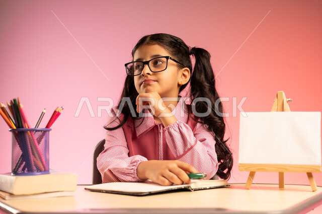 الجد والاجتهاد للوصول إلى النجاح والتفوق، موسم العودة إلى المدارس، بورتريه لطالبة عربية خليجية سعودية ترتدي الزي المدرسي ونظارة طبية تجلس في مقعدها تقوم بالنظر إلى الأعلى بإيماءات الاندماج والتركيز، قرطاسية مدرسية ولوحة فارغة على الطاولة المكتبية، خلفية ملونة