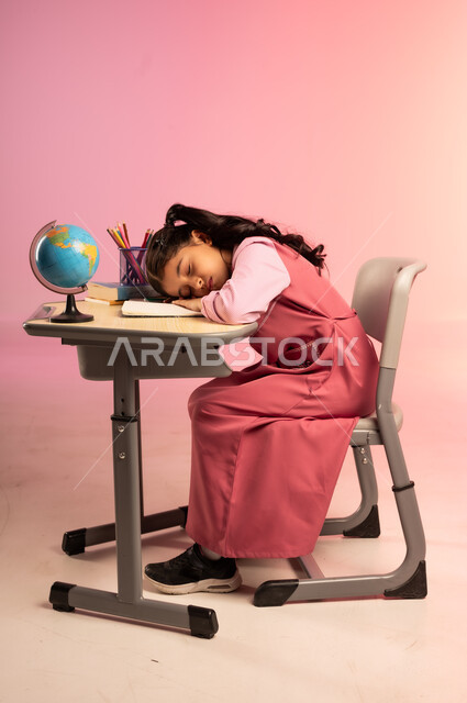 Fatigue and need for rest and sleep, school stationery and globe on desk, education in Saudi Arabia schools, back to school season, side portrait of a Saudi Arabian Gulf Arab female student wearing official school uniform sitting in her seat and taking a nap, colorful background