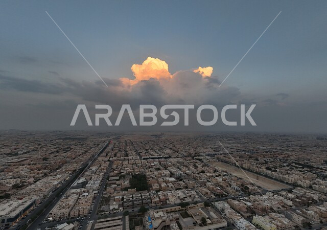 النمو والتطور العمراني في المملكة العربية السعودية، صورة جوية من طائرة درون للفن الهندسي المعماري لمدينة الرياض في وقت الغروب، الأبراج وناطحات السحاب والمنشآت والمباني التجارية، التقدم الحضاري في المدن والأحياء، خلفية السماء الملبدة بالغيوم الكثثيفة الكبيرة