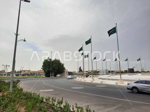 المعالم السياحية في النهار في مدينة جدة, رفرفة أعلام المملكة العربية السعودية الخضراء عند تقاطع طريق الكورنيش, الواجهة البحرية الهادئة, منظر الغيوم في السماء