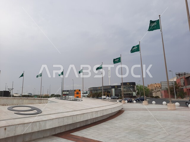 المعالم السياحية في النهار في مدينة جدة, رفرفة أعلام المملكة العربية السعودية الخضراء عند تقاطع طريق الكورنيش, الواجهة البحرية الهادئة, منظر الغيوم في السماء