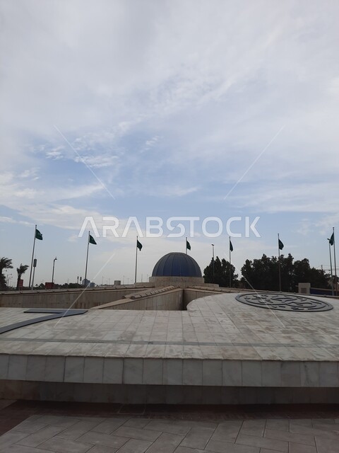 المعالم السياحية في النهار في مدينة جدة, رفرفة أعلام المملكة العربية السعودية الخضراء عند تقاطع طريق الكورنيش, الواجهة البحرية الهادئة, منظر الغيوم في السماء