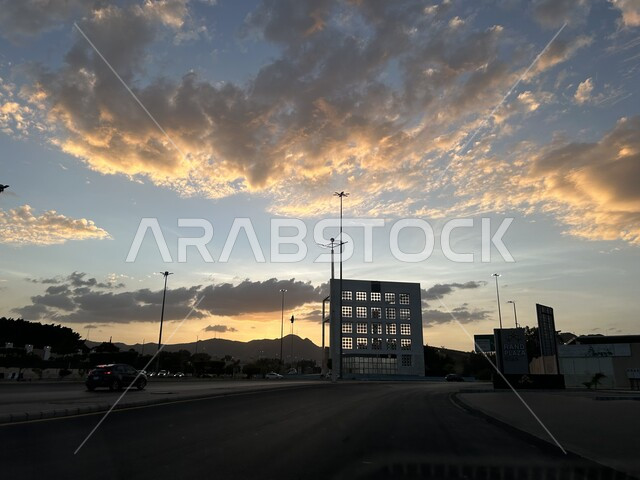 دوار المؤية في حي الخالدية، النمو والتطور الحضاري والعمراني في المملكة العربية السعودية، حركة المرور والسيارات في شارع اسفلتي معبد في طريق الهدا، معالم مدينة الطائف المشهورة، خلفية السماء الملبدة بالغيوم في وقت الغروب