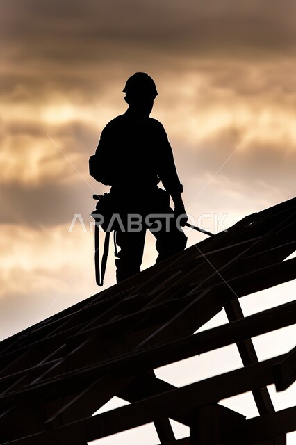 Supervising the work of heavy machinery and equipment, using cranes and scaffolding on construction sites, industrial engineering jobs in Saudi Arabia, silhouette of a Saudi Arabian Gulf construction worker wearing a helmet and safety vest standing on the roof of a building, Saluit