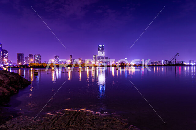 Attractions and tourist attractions, architectural engineering art in building towers and skyscrapers on Al Mamzar Beach, the coastal waterfront in Dubai, the reflection of lights and lights of hotels and buildings on the sea water at night, urban growth and development in the United Arab Emirates