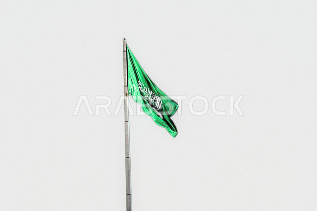 The flag of the Kingdom of Saudi Arabia flutters in the air, Flag Day and celebration of the Saudi National Day, National Day, glorifying the word of monotheism and strengthening national identity, the concept of love for the homeland and belonging to it, recalling history and showing loyalty to the country.