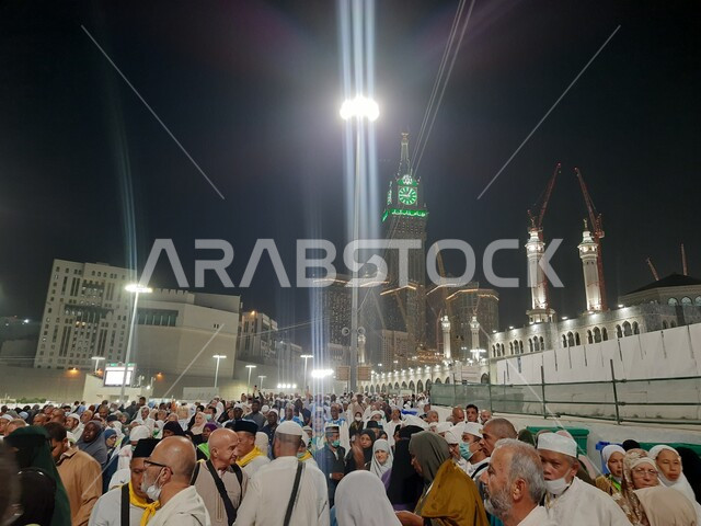 The Royal Clock Tower building in the Grand Mosque illuminated at night, pilgrims and Umrah performers in the Holy Mosque, Islamic architectural style of towers and skyscrapers in Mecca, landmarks and sacred religious places in the Kingdom of Saudi Arabia