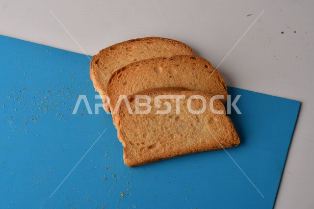 Close up of slices of toasted bread being cut on a blue cutting board, close up of fresh baked goods
