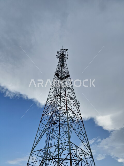 الاهتمام بتقديم الخدمات الحديثة في مدينة الطائف بالمملكة العربية السعودية، تصوير من الأسفل لبرج الاتصالات الشاهق فوق قمة جبل، خلفية السماء الزرقاء الممتلئة بالسحب والغيوم باللون الأبيض