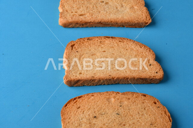 Close up of slices of toasted bread being cut on a blue cutting board, close up of fresh baked goods
