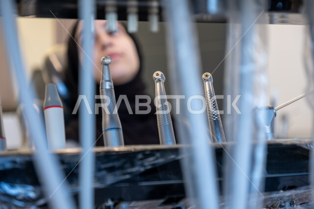  الأدوات المعقمة والأجهزة الحديثة، التقنيات المتطورة المستخدمة في العلاج، أهمية زيارة طبيب الأسنان بشكل دوري، طب وجراحة الفم والفكين، صورة لمريضة عربية خليجية سعودية محجبة تجلس على كرسي العلاج في العيادة السنية تنتظر بدء العلاج