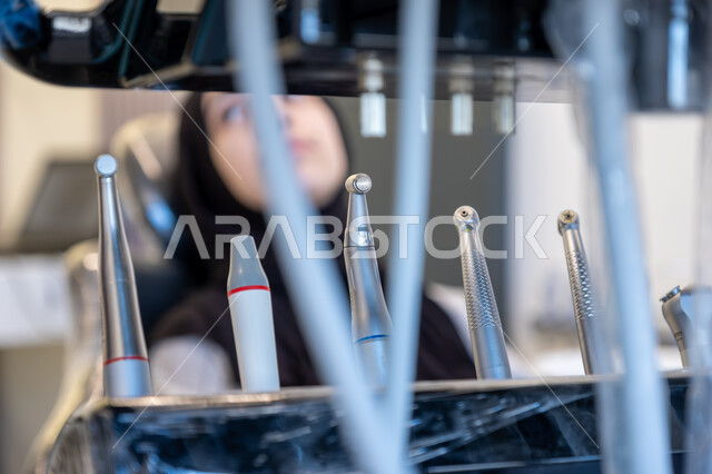  الأدوات المعقمة والأجهزة الحديثة، التقنيات المتطورة المستخدمة في العلاج، أهمية زيارة طبيب الأسنان بشكل دوري، طب وجراحة الفم والفكين، صورة لمريضة عربية خليجية سعودية محجبة تجلس على كرسي العلاج في العيادة السنية تنتظر بدء العلاج