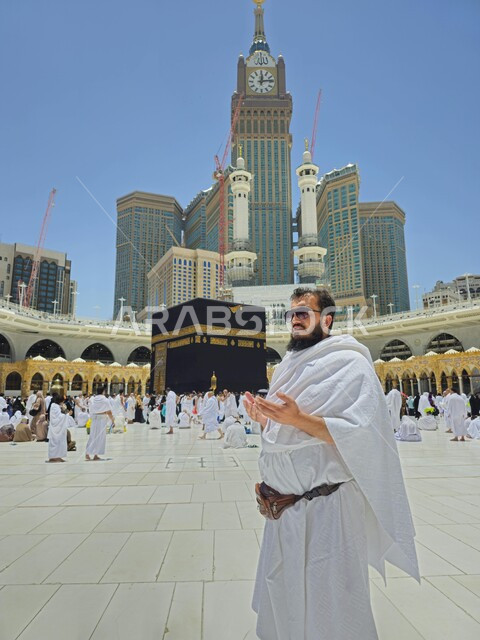 الحرم المكي الشريف في مكة المكرمة بالمملكة العربية السعودية ، أداء مناسك الحج والعمرة، معالم دينية إسلامية، الحجاج المسلمين يطوفون حول الكعبة المشرفة في مكة المكرمة، مبنى برج الساعة الملكي، أماكن إسلامية مقدسة، صورة مقربة لرجل يرفع يده للأعلى ويقوم بالدعاء 