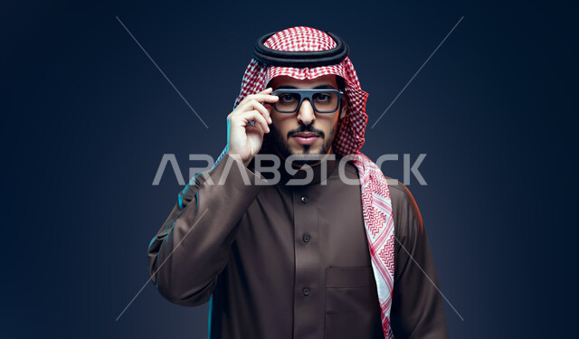 الاهتمام بالمظهر الخارجي، ارتداء النظارات الخاصة بضعف النظر, تحسين الرؤية ومحاولة تعديل البصر، بورتريه مقرب لشاب عربي خليجي سعودي يرتدي الثوب التقليدي و الشماغ يقوم بوضع النظارة الطبية, خلفية سوداء