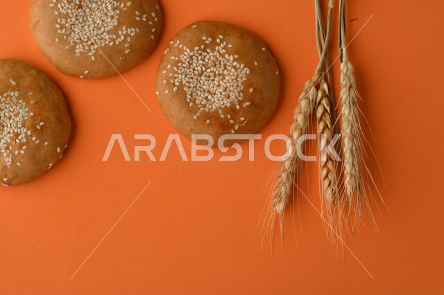 صورة مقربة لمجموعة من نباتات القمح ، وبسكويت القمح الهشة والمقرمشة على خلفية برتقالية اللون