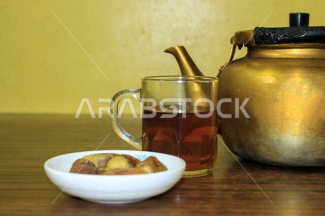 صورة لإبريق الشاي ، وطبق من التمر المليئة بالقيم الغذائية العالية ، فاكهه صيفية  ، ثمار اشجار النخيل ، كوب الشاي الأحمر ، فطور يومي