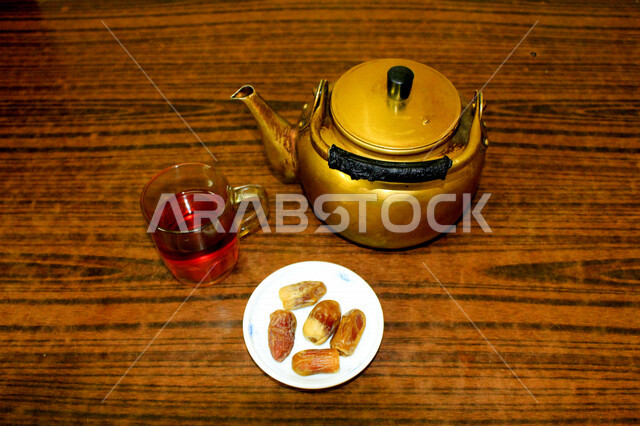 صورة لإبريق الشاي ، وطبق من التمر المليئة بالقيم الغذائية العالية ، فاكهه صيفية  ، ثمار اشجار النخيل ، كوب الشاي الأحمر ، فطور يومي