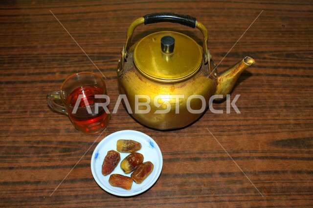 صورة لإبريق الشاي ، وطبق من التمر المليئة بالقيم الغذائية العالية ، فاكهه صيفية  ، ثمار اشجار النخيل ، كوب الشاي الأحمر ، فطور يومي